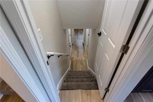 staircase featuring a textured ceiling, baseboards, and wood finished floors