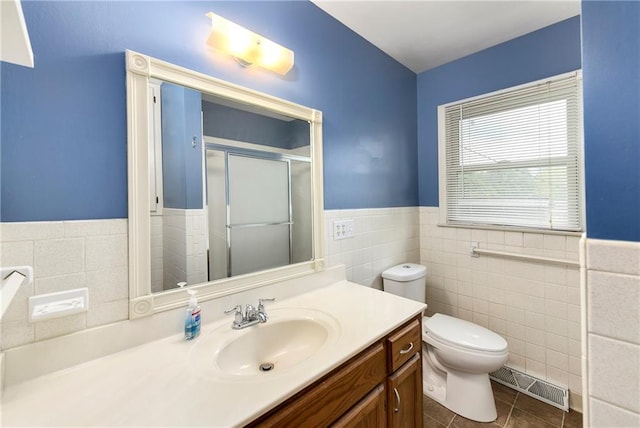 bathroom with tile walls, a shower with shower door, vanity, toilet, and tile patterned floors