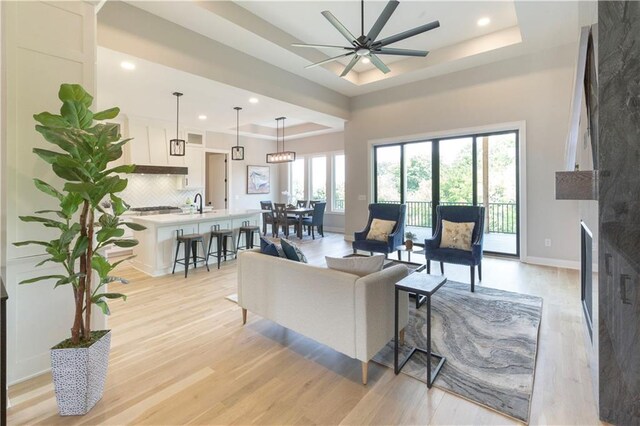 living room featuring sink, ceiling fan, light wood-type flooring, a tray ceiling, and a large fireplace