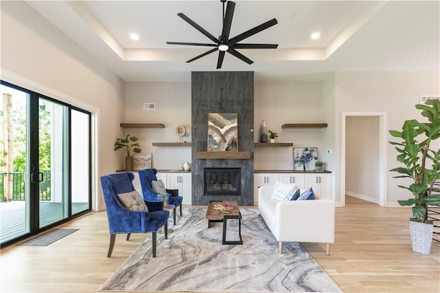 living room with a fireplace, light wood-type flooring, and a raised ceiling