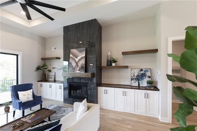 living room featuring light wood-type flooring, a large fireplace, and ceiling fan