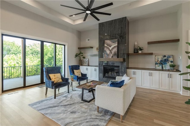 living room featuring ceiling fan, a large fireplace, and light hardwood / wood-style flooring