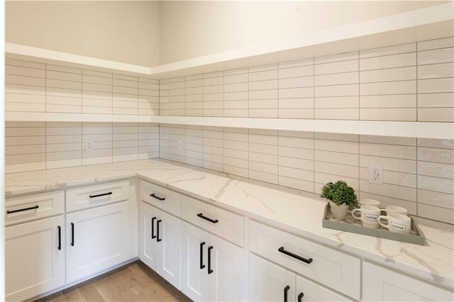 kitchen featuring decorative backsplash, white cabinetry, light stone counters, and light wood-type flooring