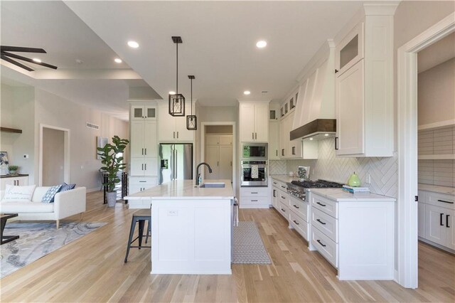 kitchen with decorative backsplash, light hardwood / wood-style flooring, an island with sink, and stainless steel appliances