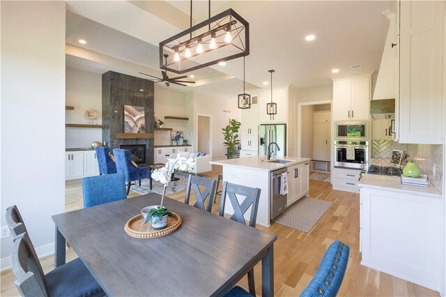 dining space with ceiling fan, light hardwood / wood-style floors, sink, and a tiled fireplace