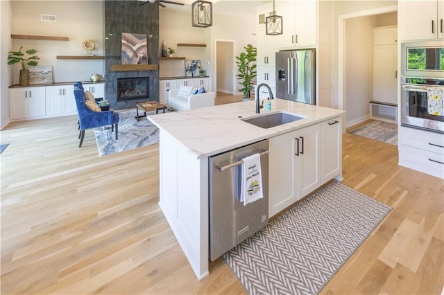 kitchen with appliances with stainless steel finishes, a kitchen island with sink, sink, pendant lighting, and white cabinets