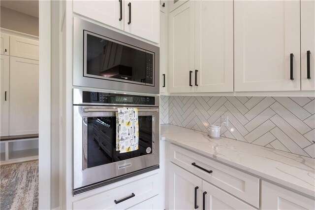 kitchen with white cabinets, stainless steel appliances, light stone counters, and tasteful backsplash