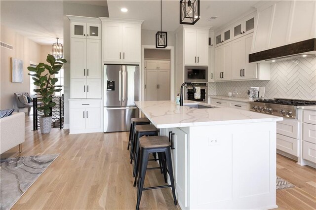 kitchen featuring stainless steel appliances, sink, pendant lighting, a center island with sink, and light hardwood / wood-style floors