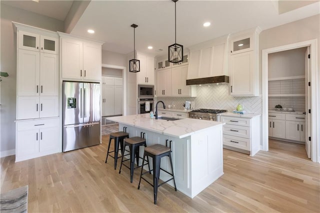 kitchen featuring white cabinetry, sink, hanging light fixtures, stainless steel appliances, and a center island with sink