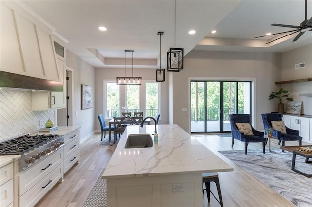 kitchen with a center island with sink, white cabinetry, a healthy amount of sunlight, and sink