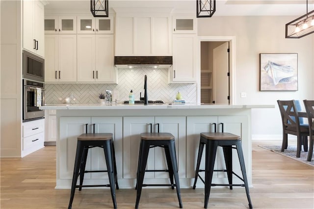 kitchen with pendant lighting, an island with sink, a kitchen bar, white cabinetry, and stainless steel appliances