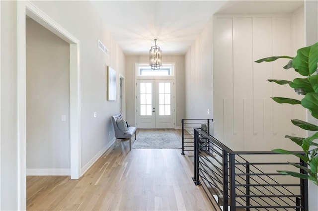 foyer entrance with french doors, light hardwood / wood-style floors, and an inviting chandelier