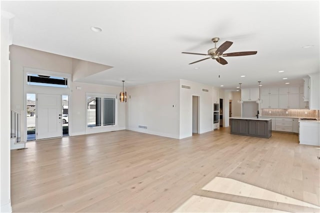 unfurnished living room featuring sink, light hardwood / wood-style flooring, and ceiling fan with notable chandelier