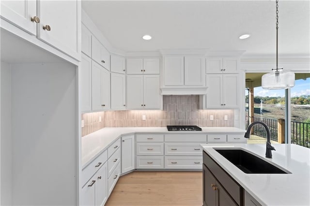 kitchen with white cabinets, light stone counters, black gas stovetop, sink, and decorative light fixtures