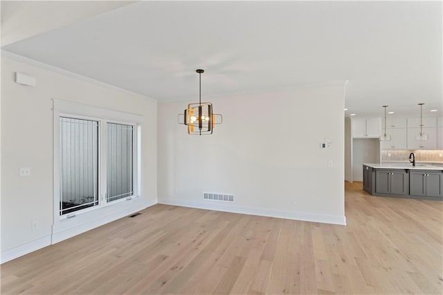 unfurnished dining area with ornamental molding, sink, light hardwood / wood-style flooring, and a notable chandelier