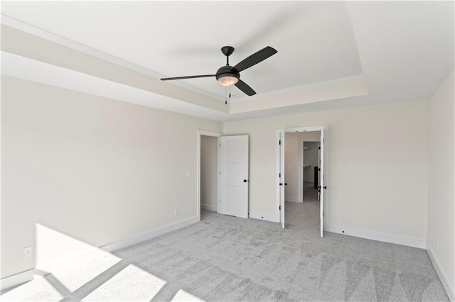 unfurnished bedroom featuring ceiling fan, a tray ceiling, a walk in closet, and light colored carpet