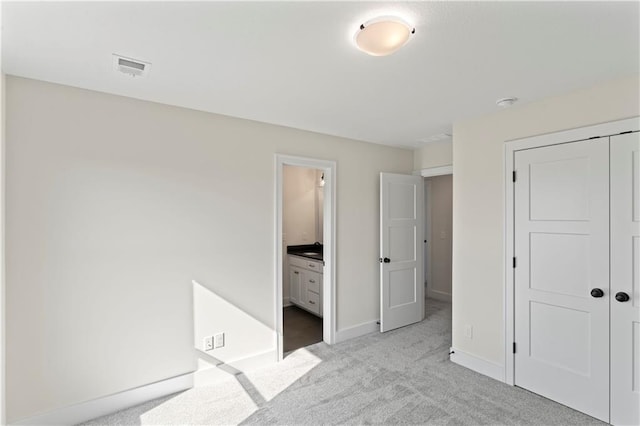 unfurnished bedroom featuring light carpet, ensuite bathroom, and a closet