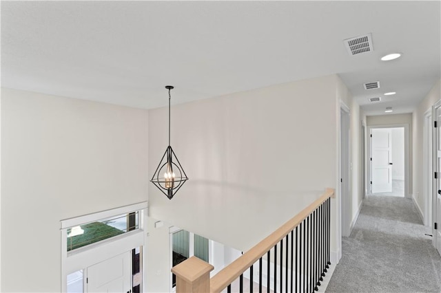 corridor with a notable chandelier and light colored carpet