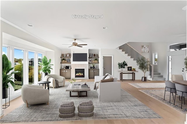 7075 NW Magnus Ct, Parkville, MO 64152 - living room with stairs, a lit fireplace, wood finished floors, ceiling fan, and built in shelves