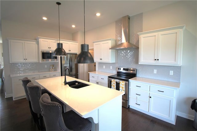 kitchen with appliances with stainless steel finishes, an island with sink, sink, white cabinets, and wall chimney exhaust hood