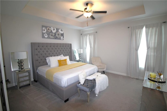 bedroom with a tray ceiling, dark carpet, and multiple windows