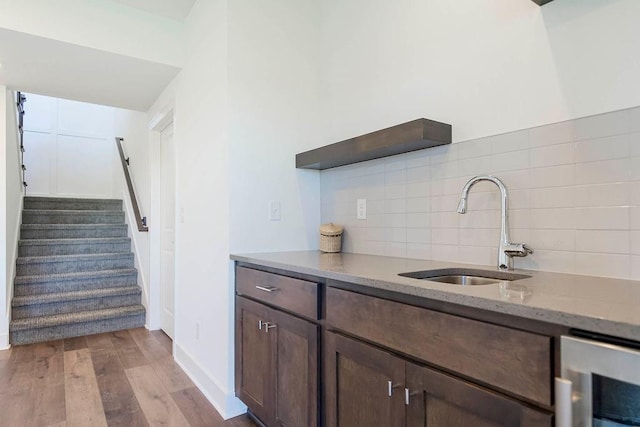 kitchen featuring wine cooler, dark brown cabinetry, sink, tasteful backsplash, and light hardwood / wood-style flooring