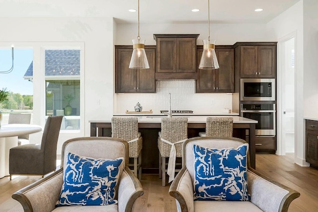 kitchen with built in microwave, oven, backsplash, hanging light fixtures, and a kitchen island with sink