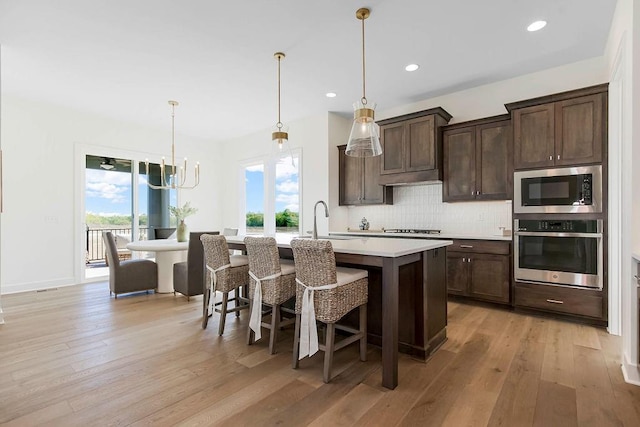 kitchen featuring stainless steel appliances, an island with sink, sink, and decorative light fixtures