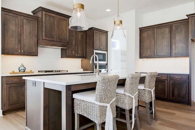 kitchen featuring built in microwave, an island with sink, sink, hanging light fixtures, and light hardwood / wood-style flooring