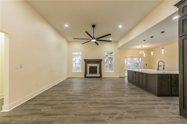 unfurnished living room with dark hardwood / wood-style flooring, sink, a stone fireplace, and ceiling fan