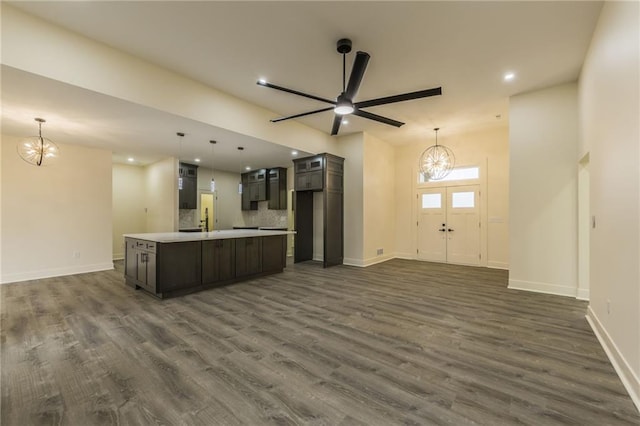 kitchen featuring dark hardwood / wood-style floors, ceiling fan with notable chandelier, an island with sink, decorative backsplash, and hanging light fixtures