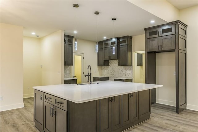 kitchen featuring decorative backsplash, an island with sink, sink, and hanging light fixtures