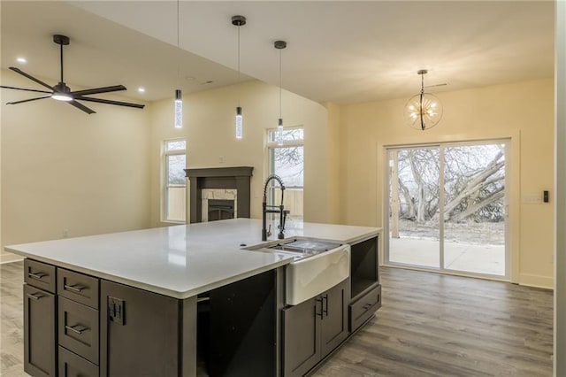 kitchen featuring sink, a kitchen island with sink, light hardwood / wood-style floors, a stone fireplace, and decorative light fixtures