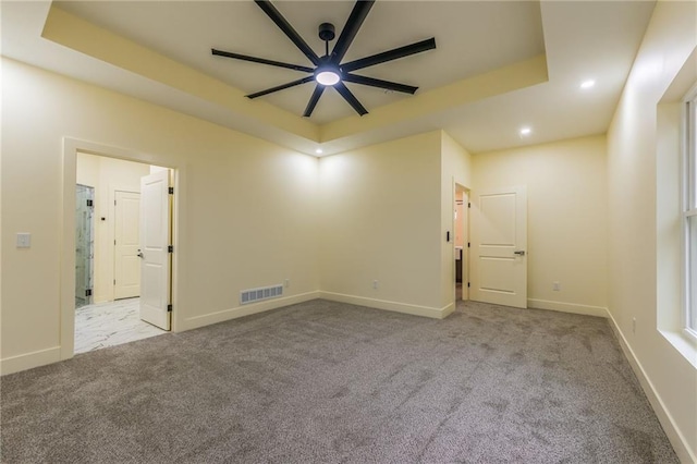 unfurnished room with ceiling fan, light colored carpet, and a tray ceiling