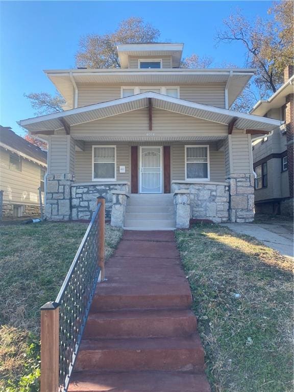 american foursquare style home featuring covered porch and stone siding