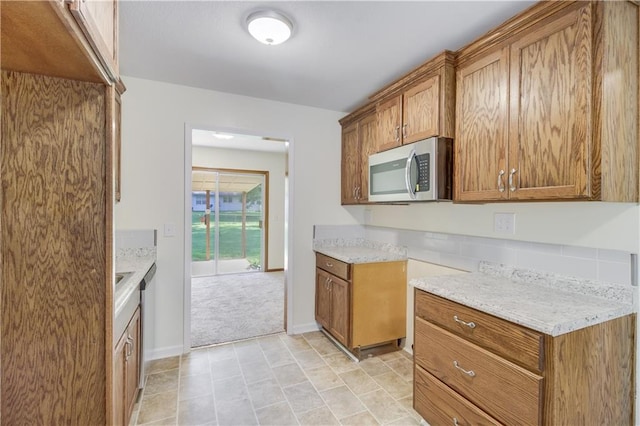 kitchen featuring light carpet, stainless steel appliances, baseboards, light stone countertops, and brown cabinetry