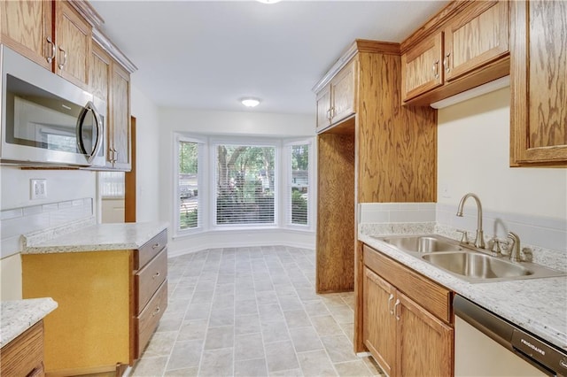 kitchen with baseboards, brown cabinetry, light stone counters, stainless steel appliances, and a sink