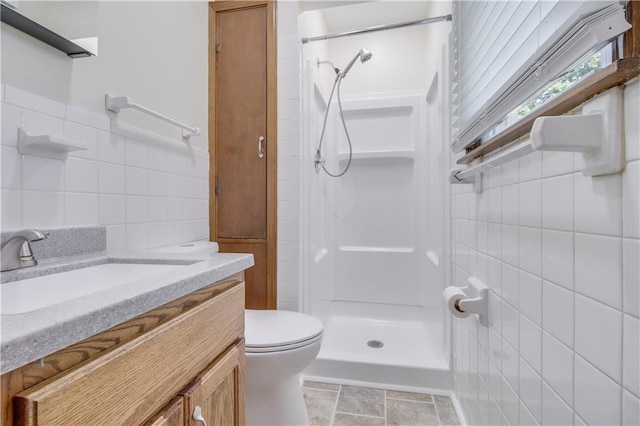 bathroom featuring toilet, a shower stall, tile walls, and vanity