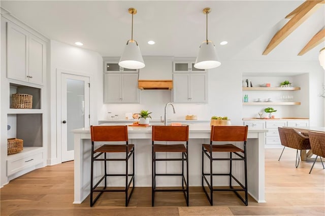 kitchen featuring a kitchen island with sink, light wood-style flooring, light countertops, and open shelves