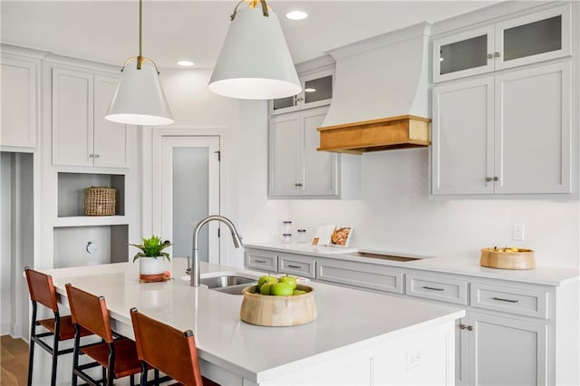 kitchen featuring a kitchen island with sink, a sink, light countertops, black electric cooktop, and custom exhaust hood