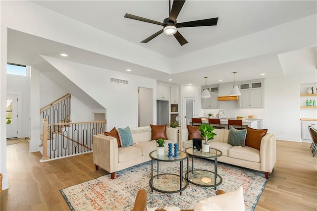 living room with visible vents, a tray ceiling, recessed lighting, light wood-style floors, and stairs