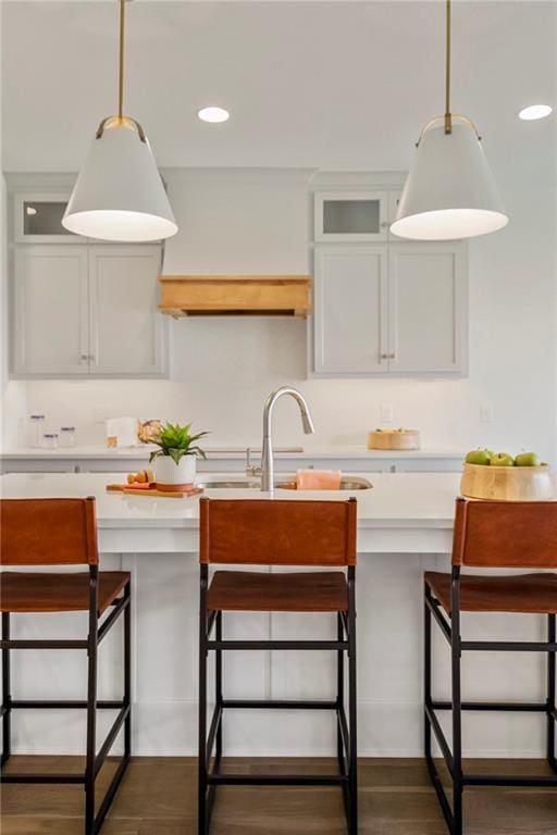 kitchen featuring a sink, hanging light fixtures, light countertops, glass insert cabinets, and a kitchen breakfast bar