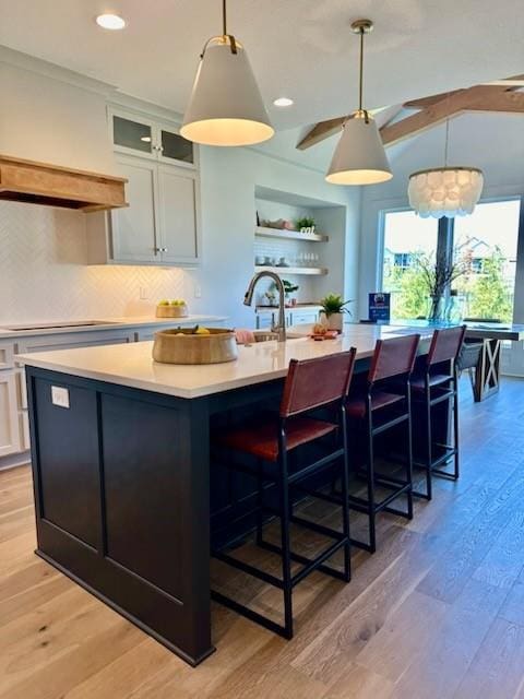 kitchen featuring light wood-style flooring, stovetop, an island with sink, and light countertops