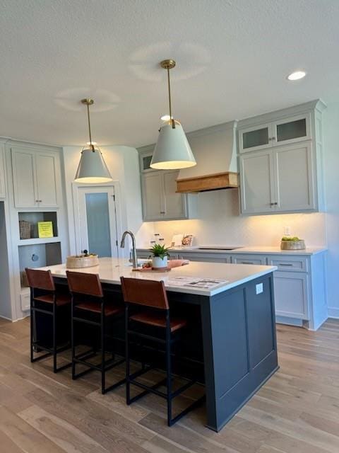 kitchen featuring light countertops, custom range hood, light wood-style floors, and a kitchen breakfast bar