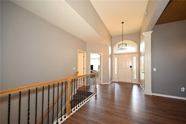 foyer entrance with dark hardwood / wood-style floors, a towering ceiling, a chandelier, and decorative columns