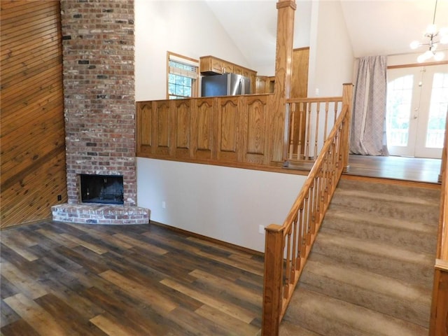 stairway featuring an inviting chandelier, a brick fireplace, wood-type flooring, and high vaulted ceiling