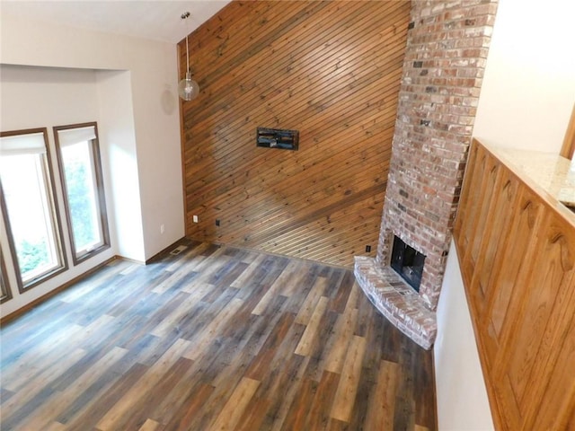 unfurnished living room with a brick fireplace, dark hardwood / wood-style floors, and wooden walls