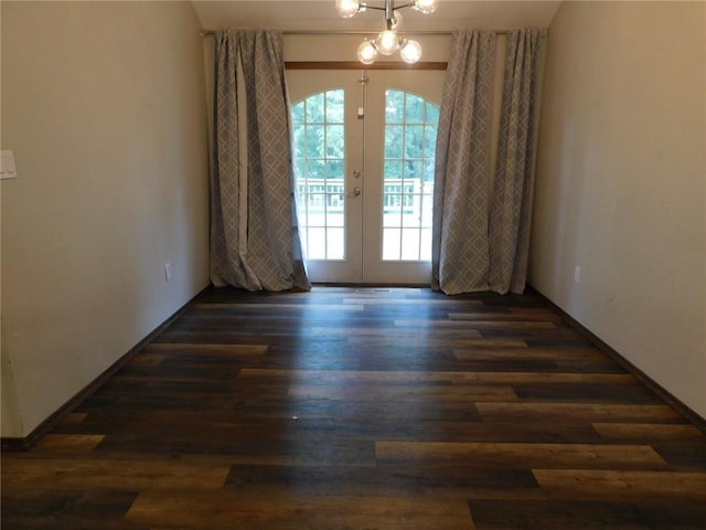 spare room with french doors, dark hardwood / wood-style flooring, and an inviting chandelier