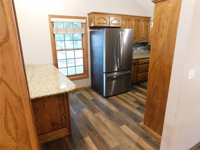 kitchen with lofted ceiling, dark wood-type flooring, stainless steel refrigerator, light stone counters, and tasteful backsplash