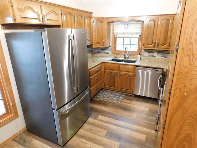 kitchen with sink, light stone counters, appliances with stainless steel finishes, light hardwood / wood-style floors, and backsplash